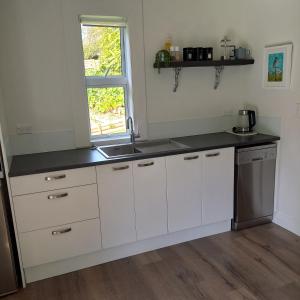 a kitchen with white cabinets and a sink and a window at Hahei Cottages - Willow or Kauri in Hahei