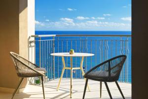 a table and chairs on a balcony with the ocean at Malta Marriott Resort & Spa in St. Julianʼs