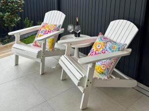 deux chaises blanches avec des coussins assis à côté d'une table dans l'établissement Casa Dis Family Friendly 350m walk to beach, à Caves Beach