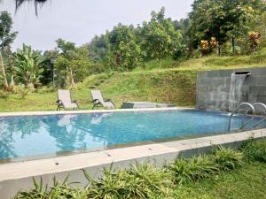 a swimming pool with two chairs next to a hill at Kebun Teduh Sukaharja Cijeruk Bogor in Palasari