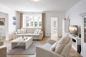 Una sala de estar con muebles blancos y un televisor. en Villa Maiken, en Wyk auf Föhr