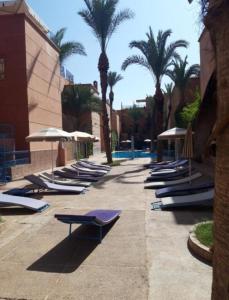 a row of lounge chairs with umbrellas and palm trees at Riad Dar Fatna in Marrakesh