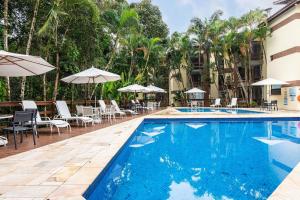 a swimming pool with chairs and umbrellas next to a building at Riviera Green - Premium Two in Riviera de São Lourenço