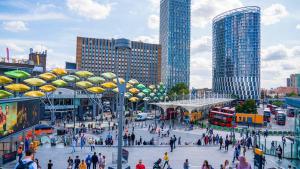 a crowd of people walking in a city with tall buildings at Stratford- in London