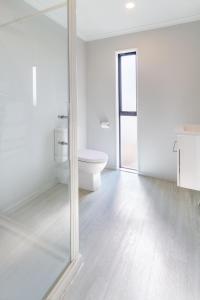 La salle de bains blanche est pourvue de toilettes et d'une porte en verre. dans l'établissement Wigram Escape Minutes to Ngā Puna Wai Sports Hub, à Christchurch