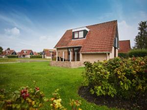 a house with a red roof on a green yard at Holiday Home in Zeeland near Beaches in Heinkensand