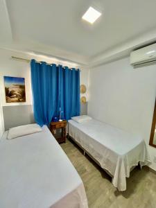 two beds in a room with blue curtains at Apê Vumbora Pra Praia, todo climatizado, a 200 m da praia in Ilhéus