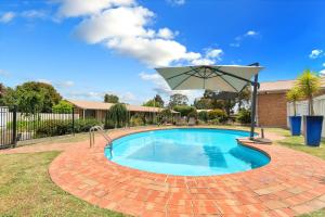 una piscina con sombrilla en un patio en Begonia City Motor Inn, en Ballarat