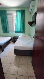een slaapkamer met 2 bedden en een raam met groene gordijnen bij Praia Grande Boqueirão e Guilhermina in Praia Grande