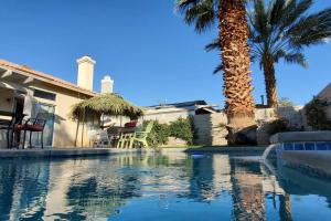 a swimming pool in front of a house with palm trees at Sunshine Daydream by the Pool and Spa in Indio