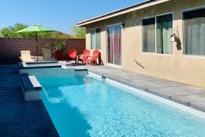 a swimming pool with red chairs and an umbrella at Happy Hour & Sunshine in Indio