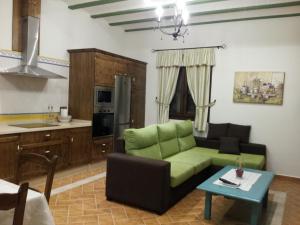 sala de estar con sofá verde y cocina en Casa Rural con jacuzzi y pista de padel - Casa de Pacas, en Bolaños de Calatrava
