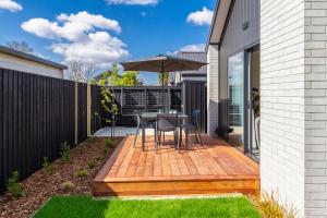 a wooden deck with a table and an umbrella at The Kind Kiwi A brand new home in Riccarton in Christchurch