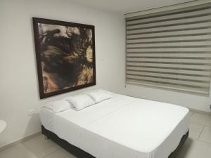a bedroom with a white bed with a painting on the wall at Alojamiento maraya in Pereira