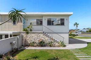 a white house with a stone wall and stairs at Pacific Breeze in Caves Beach