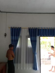 a man standing in a room with blue curtains at Homestay Saptia Dewi in Sengkol
