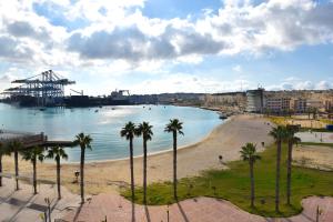 a beach with palm trees in front of a harbor at Pretty Bay Apartments in Birżebbuġa