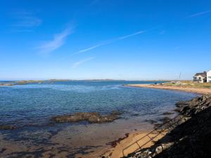 a body of water with a beach and a house at Tides Reach in Rhosneigr