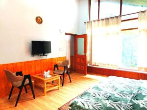 sala de estar con cama, sillas y TV en Melody Orchard Cottage, en Jagatsukh