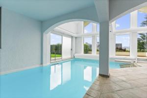 a swimming pool with blue water in a building with windows at Villa de lujo y piscina climatizada in Puente Arce