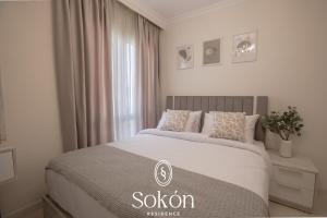a white bedroom with a bed with a window at Luxury 2BR City View Sokón R in Madinaty