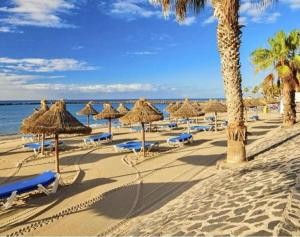 einen Strand mit Strohschirmen und -stühlen und dem Meer in der Unterkunft BLUEBIRD Luxury apartment in Las Americas in Playa de las Americas