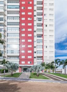 a red building with palm trees in front of it at PALMAS EXPERIENCE - APARTAMENTO CONTEMPORÂNEO, vista serra, na quadra do shopping in Palmas