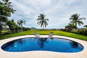 a swimming pool with two chairs and palm trees at Beachfront Hideaway with Pool & Ocean Views in Playa Flamingo