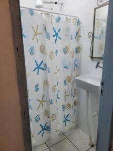 a bathroom with a shower curtain with seashells and a sink at Casinha Grão de Areia de frente para o mar in Bertioga