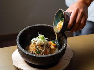 a person pouring sauce into a bowl of food at Glamday Style Okinawa Yomitan Hotel & Resort in Yomitan