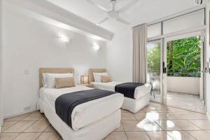a white bedroom with two beds and a window at The MAGNA by Reef Stays in Palm Cove