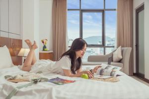 a woman laying on a bed reading a book at Star Hotel and Spa Danang in Danang