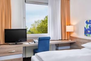 una camera da letto con una scrivania con una televisione e una sedia blu di H+ Hotel Frankfurt Airport West a Hofheim am Taunus