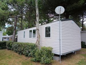 a white tiny house sitting next to a tree at MH F52 Camping Bois Masson in Saint-Jean-de-Monts