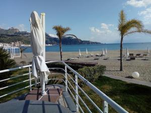 a beach with a white umbrella and chairs and boats at Sileno Beach Giardini Naxos in Giardini Naxos +10 photos