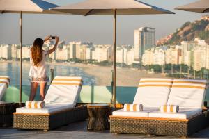 a young girl standing on a balcony with chairs and an umbrella at PortoBay Rio de Janeiro in Rio de Janeiro