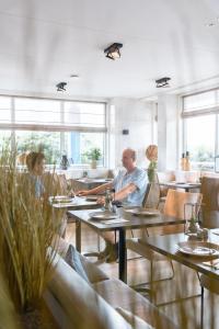 Un uomo e una donna seduti ai tavoli in un ristorante di Strandhotel Buren aan Zee a Buren