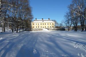 un grand bâtiment blanc dans la neige avec des arbres dans l'établissement Åkeshofs Slott, à Stockholm