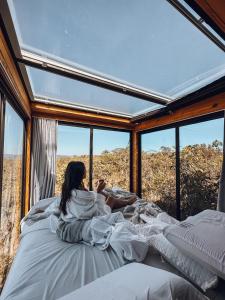 a woman laying in bed in a room with windows at Refúgio Veadeiros Container in Sao Jorge