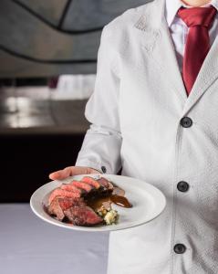 a man holding a plate of food with a piece of meat at The Evelyn NoMad in New York