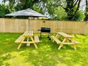 two picnic tables and a grill with an umbrella at 5-Bedroom Cottage in New Waltham, Grimsby in Grimsby