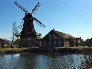 a windmill in front of a building next to a river at Mühlenhof Nesse in Dornum
