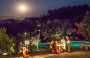 a group of people sitting at tables on a patio at night at Armonia Bay Hotel in Kokkari