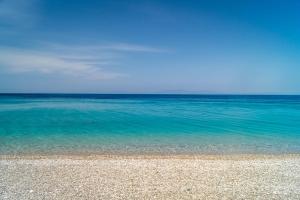 a beach with the ocean and blue water at Armonia Bay Hotel in Kokkari
