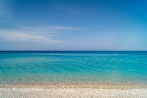 a beach with blue water and a blue sky at Armonia Bay Hotel in Kokkari