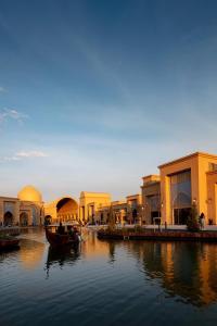 a group of buildings next to a river with boats at KARAVANSARAY Turkistan Family Hotel - FLYING THEATRE ACCESS in Türkistan