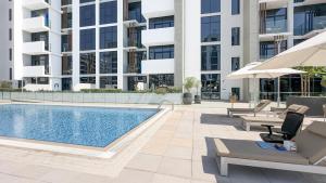 Escape24 Stylish Studio Azizi Riviera 8 Meydan one Dubai في دبي: مسبح وكراسي صالة ومبنى