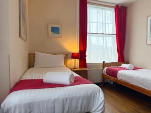 two beds in a room with red curtains and a window at The Western in St Ives