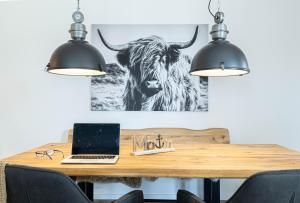 Ein Laptop auf einem Holztisch, an der Wand ein Kuhbild. in der Unterkunft Ferienwohnung Wiking-Koje 2 Schleswig in Schleswig