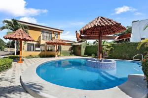a swimming pool with an umbrella in front of a house at Villa with Pool, Gated Playas del Coco Getaway in Coco